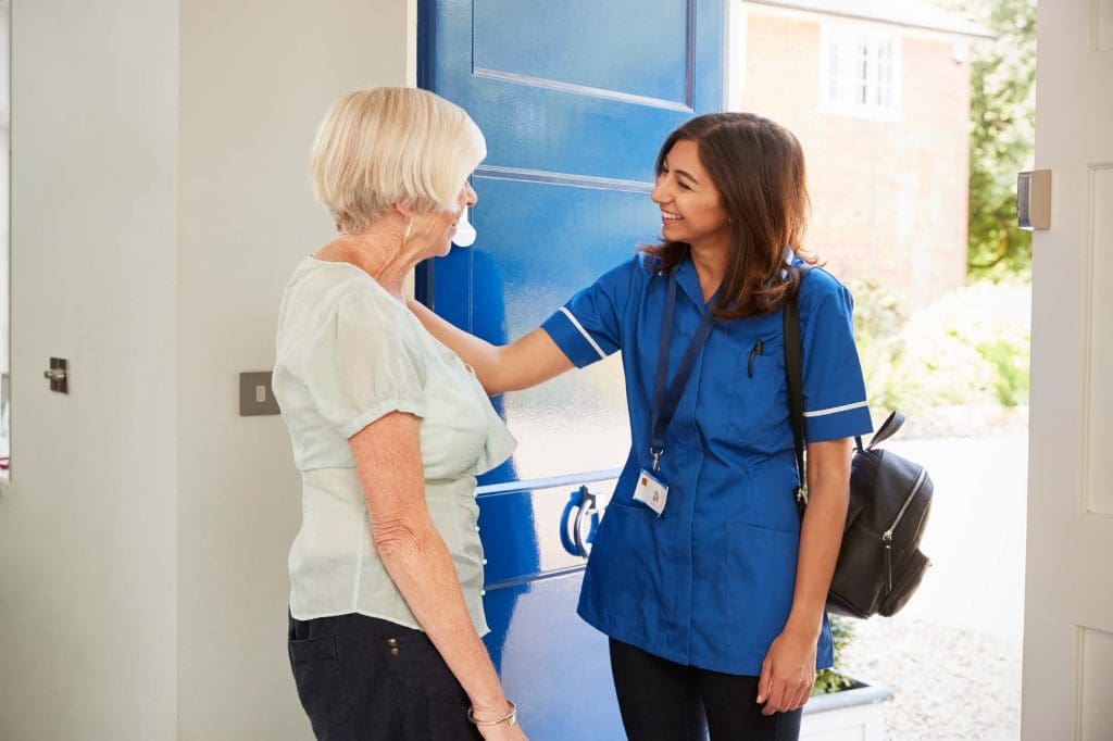 Nurse on home visit greets senior woman at her front door